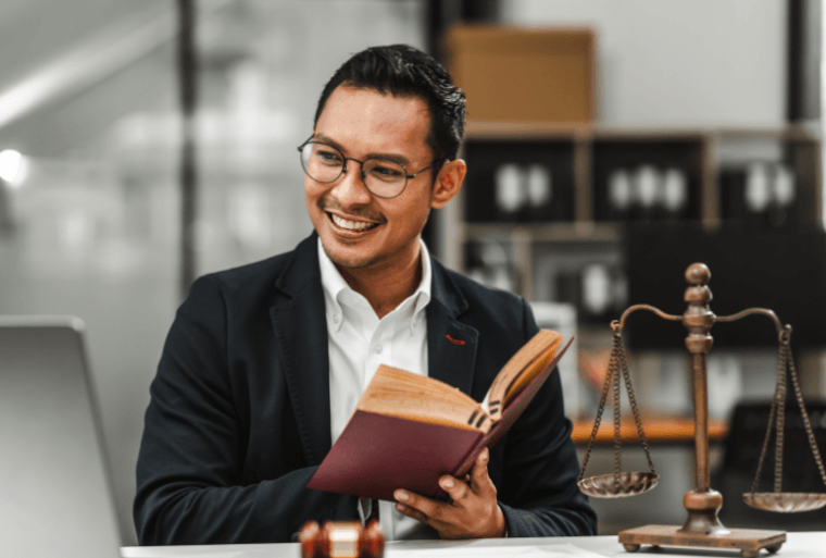 Smiling man reading a book with justice scales on desk.