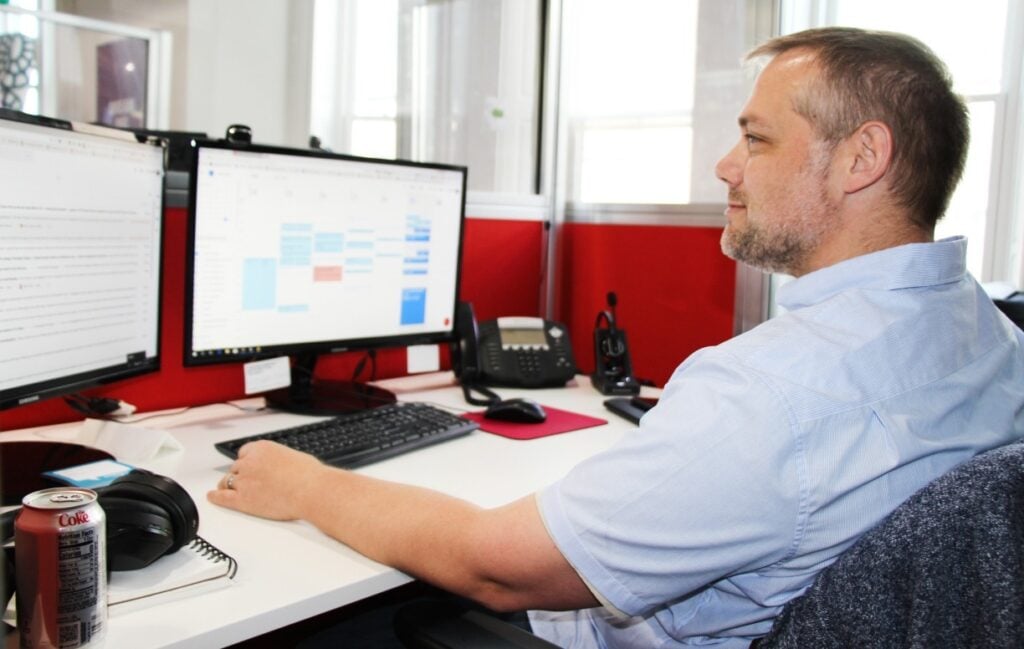 Man at work desk with dual monitors.