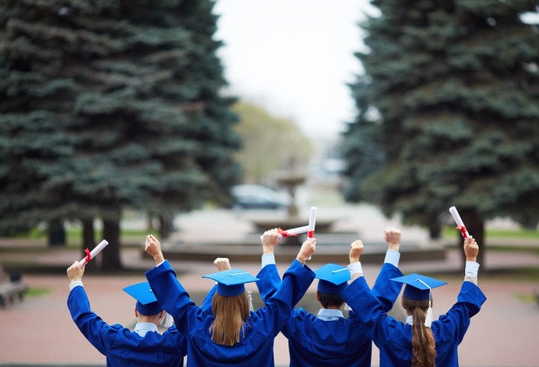 Graduates with caps up, diplomas in hand, celebrating.