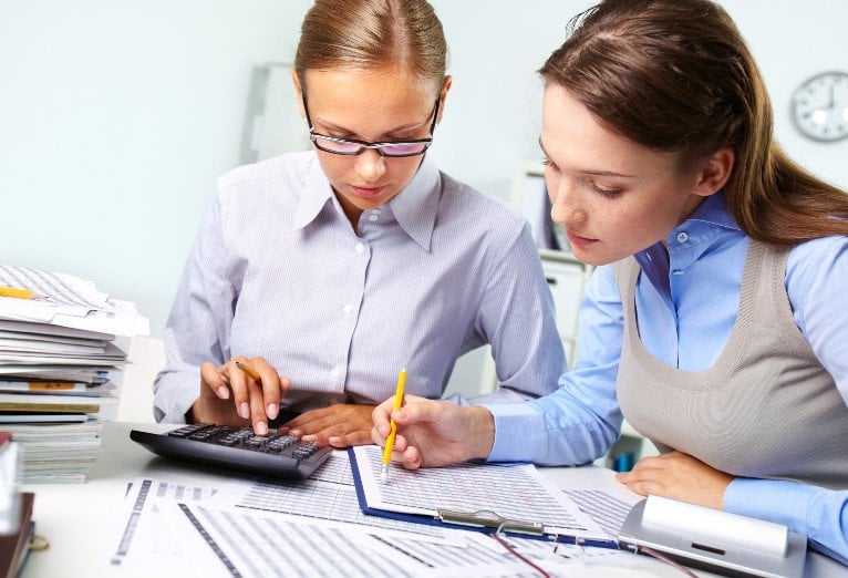 a woman is using a calculator while another woman writes on a clipboard