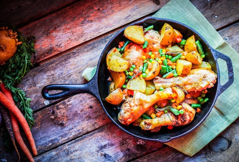 Roasted chicken and vegetables in a skillet on a wooden table.