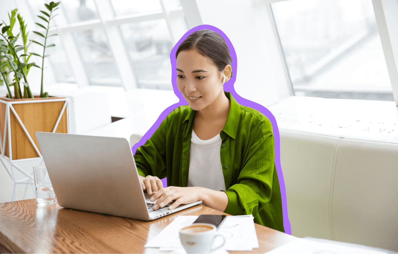 Woman in a green top sitting at a table, scrolling on a laptop