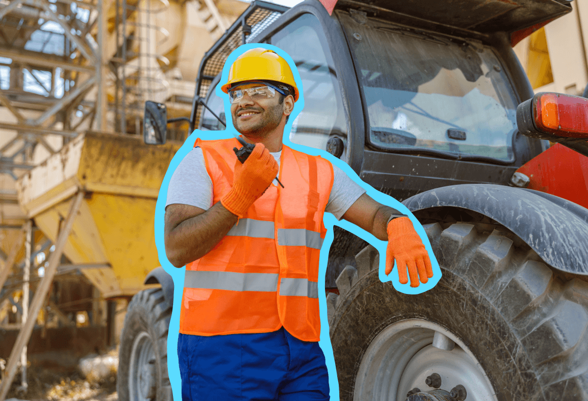 Construction worker in a safety vest leaning on a piece of heavy equipment while talking in a radio